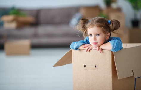 Child girl sitting in box for moving to new apartment