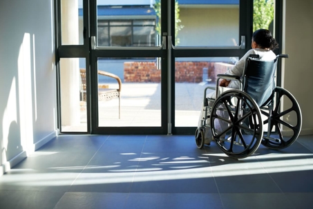 An old woman sitting in a wheelchair at the the door of a nursing home.