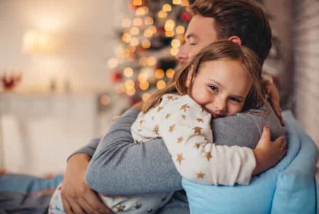 father and daughter hugging in front of a christmas tree