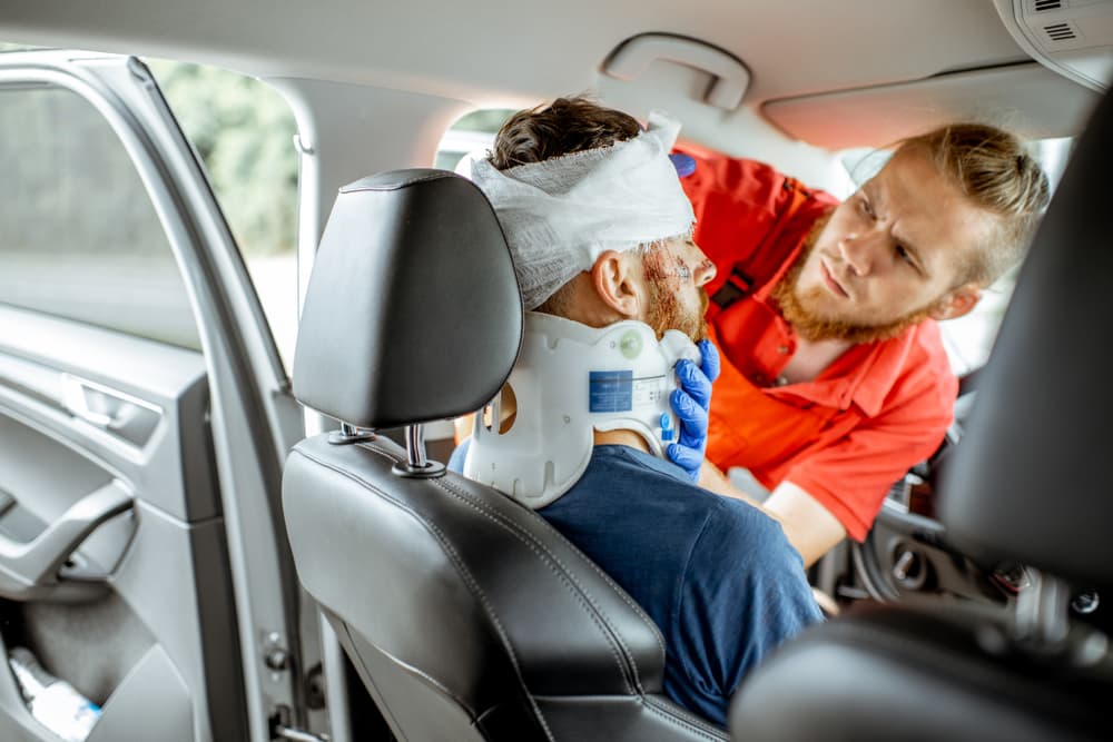 Paramedic applying bandage to the injured victim's head while seated in the driver's seat after a road accident.