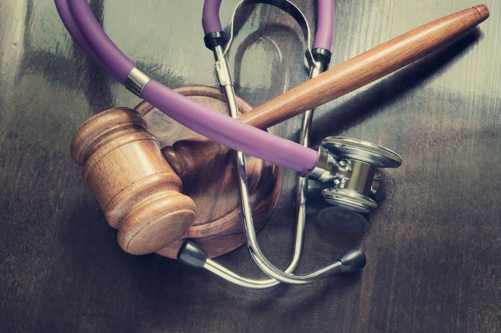 A gavel and stethoscope placed on a wooden table, symbolizing the intersection of law and medicine.